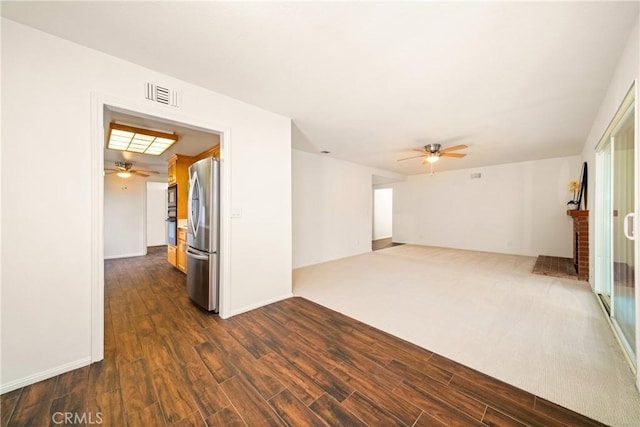 spare room with a brick fireplace, dark wood-type flooring, and ceiling fan