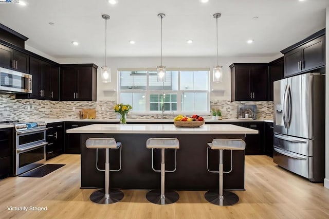 kitchen with hanging light fixtures, appliances with stainless steel finishes, a center island, and light wood-type flooring