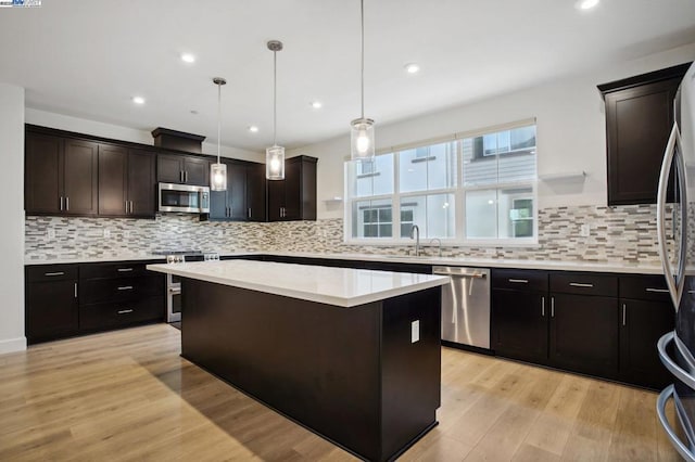 kitchen with sink, stainless steel appliances, dark brown cabinetry, a kitchen island, and decorative light fixtures