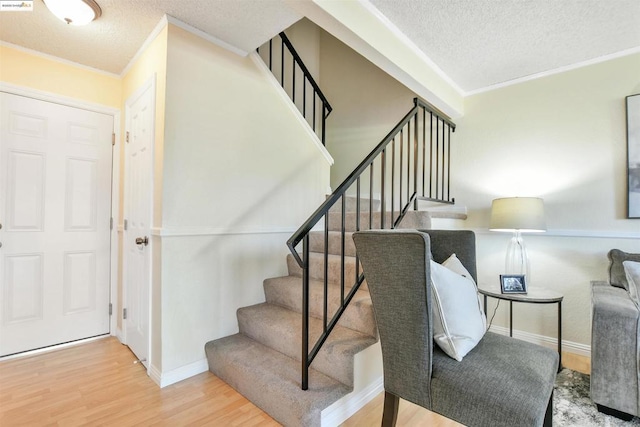 stairway with crown molding, wood-type flooring, and a textured ceiling