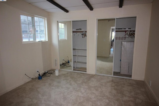 unfurnished bedroom with two closets, beamed ceiling, and carpet flooring