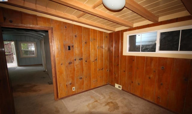 carpeted spare room featuring wooden walls and beamed ceiling