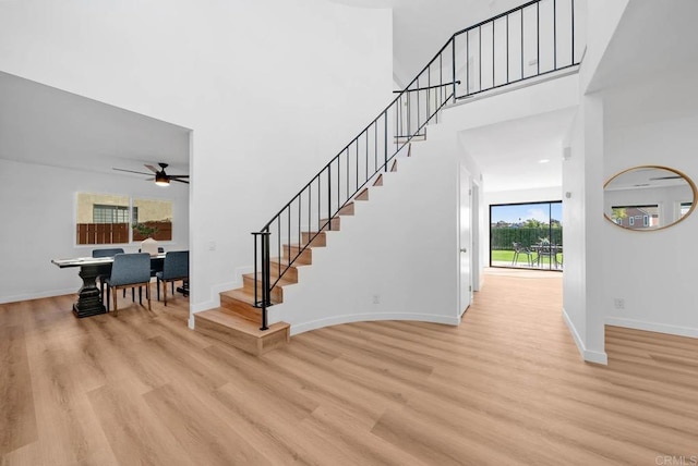 staircase with ceiling fan, wood-type flooring, and a high ceiling