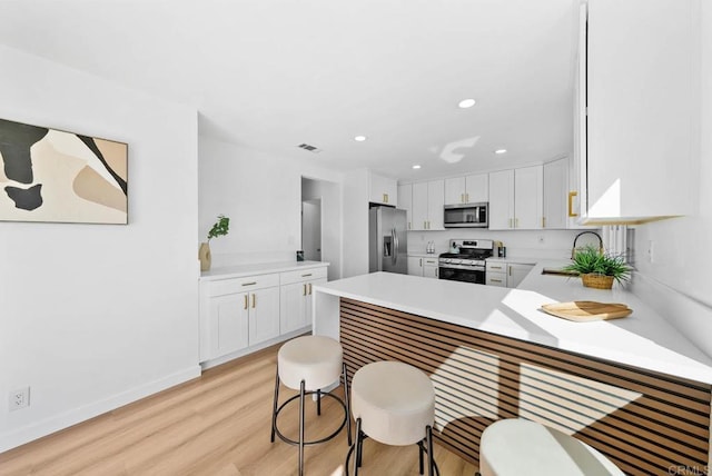 kitchen with sink, light hardwood / wood-style flooring, kitchen peninsula, stainless steel appliances, and white cabinets