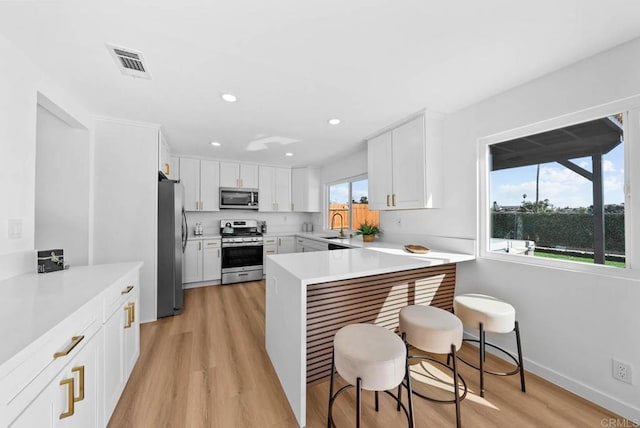 kitchen with a kitchen bar, white cabinetry, light wood-type flooring, appliances with stainless steel finishes, and kitchen peninsula