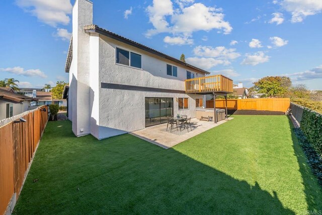 back of house featuring a hot tub, a patio, a deck, and a lawn