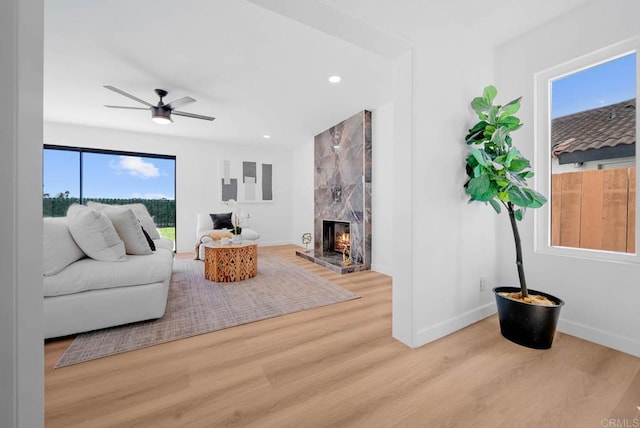 living room featuring a high end fireplace, ceiling fan, and light wood-type flooring