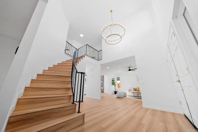 stairway with a towering ceiling, wood-type flooring, and ceiling fan with notable chandelier