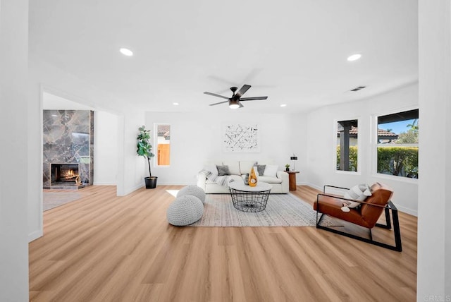 living room with a premium fireplace, ceiling fan, and light wood-type flooring