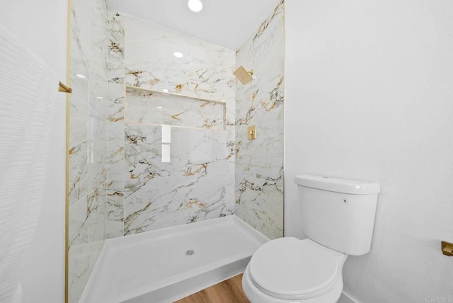 bathroom with hardwood / wood-style flooring, a tile shower, and toilet