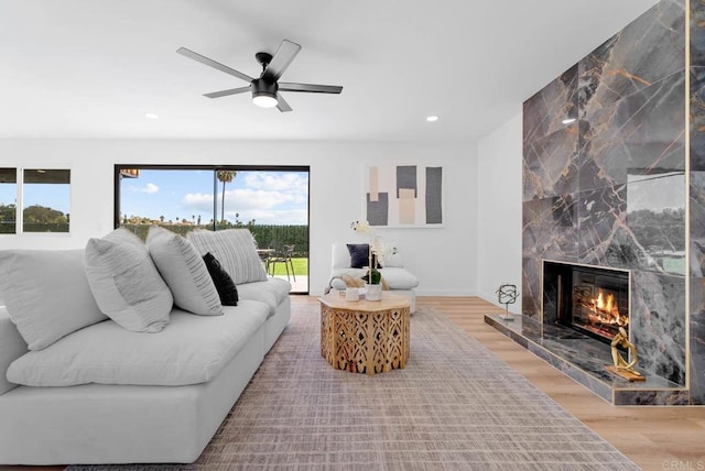 living room featuring ceiling fan, a high end fireplace, and light wood-type flooring