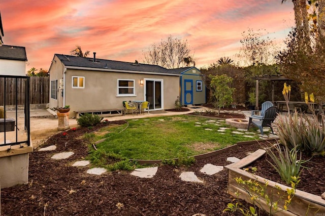 back house at dusk featuring a fire pit, a lawn, an outdoor structure, and a patio area