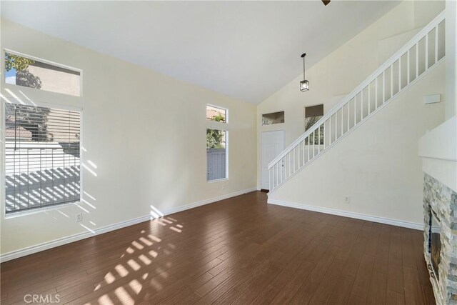 unfurnished living room featuring dark wood-type flooring, a stone fireplace, and high vaulted ceiling