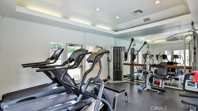 gym with a tray ceiling and a healthy amount of sunlight