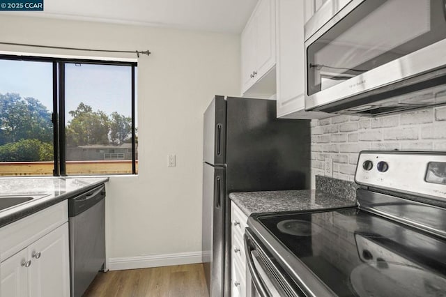 kitchen with stainless steel appliances, white cabinetry, light stone countertops, and light wood-type flooring