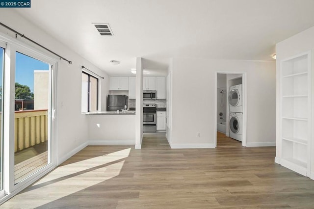 unfurnished living room featuring stacked washer and dryer, light wood-type flooring, and built in shelves