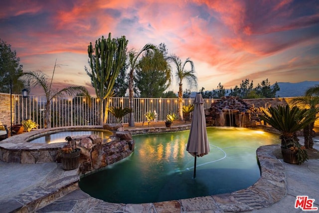 pool at dusk featuring an in ground hot tub