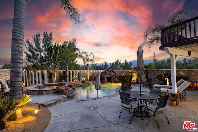 patio terrace at dusk with pool water feature, a balcony, and a pool with hot tub