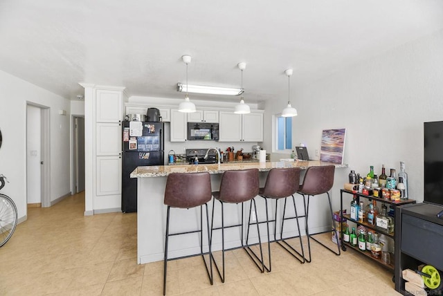 kitchen with pendant lighting, white cabinetry, a kitchen breakfast bar, black appliances, and light stone countertops