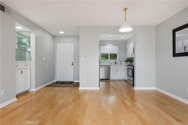 interior space with white cabinetry, sink, hanging light fixtures, stainless steel appliances, and light hardwood / wood-style flooring