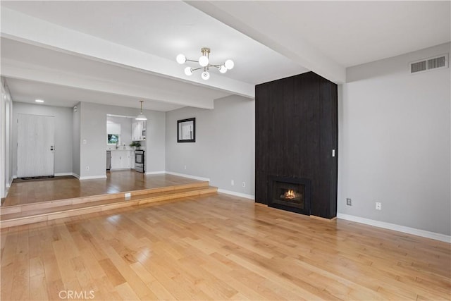 unfurnished living room with a notable chandelier, a large fireplace, beamed ceiling, and light wood-type flooring