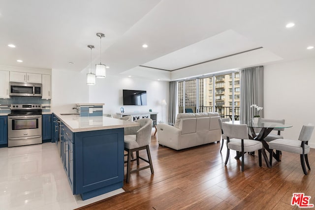 kitchen with blue cabinetry, appliances with stainless steel finishes, a raised ceiling, and hanging light fixtures