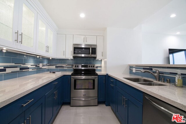 kitchen with appliances with stainless steel finishes, white cabinetry, sink, light stone counters, and blue cabinetry