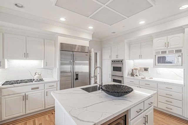 kitchen featuring light stone countertops, a kitchen island with sink, built in appliances, and white cabinets