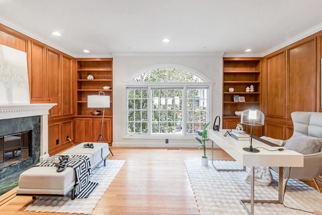 interior space with crown molding, light wood-type flooring, built in features, and a high end fireplace