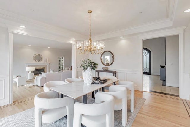 dining room featuring a premium fireplace, crown molding, light wood-type flooring, and a tray ceiling