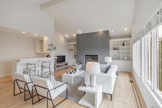 living room with built in shelves, high vaulted ceiling, a brick fireplace, light wood-type flooring, and beamed ceiling