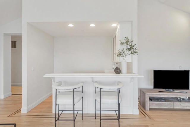 kitchen with white cabinetry, light hardwood / wood-style floors, a kitchen breakfast bar, and kitchen peninsula