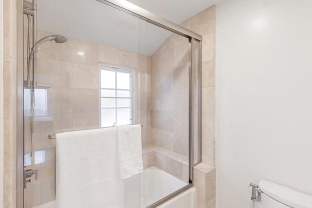 bathroom featuring bath / shower combo with glass door and toilet