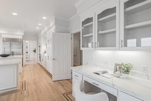 interior space featuring built in fridge, white cabinetry, ornamental molding, light stone counters, and light hardwood / wood-style floors