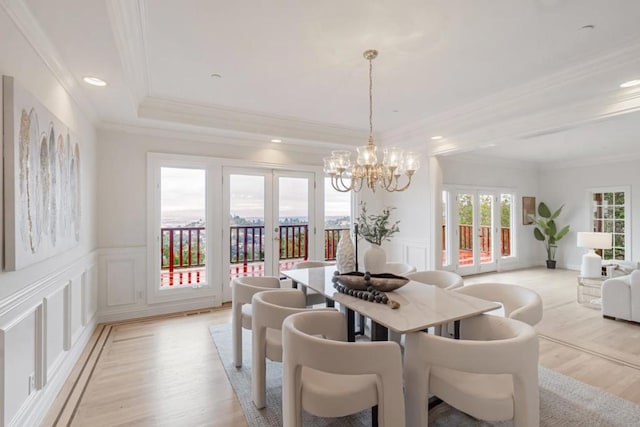 dining space with a notable chandelier, ornamental molding, a raised ceiling, french doors, and light wood-type flooring