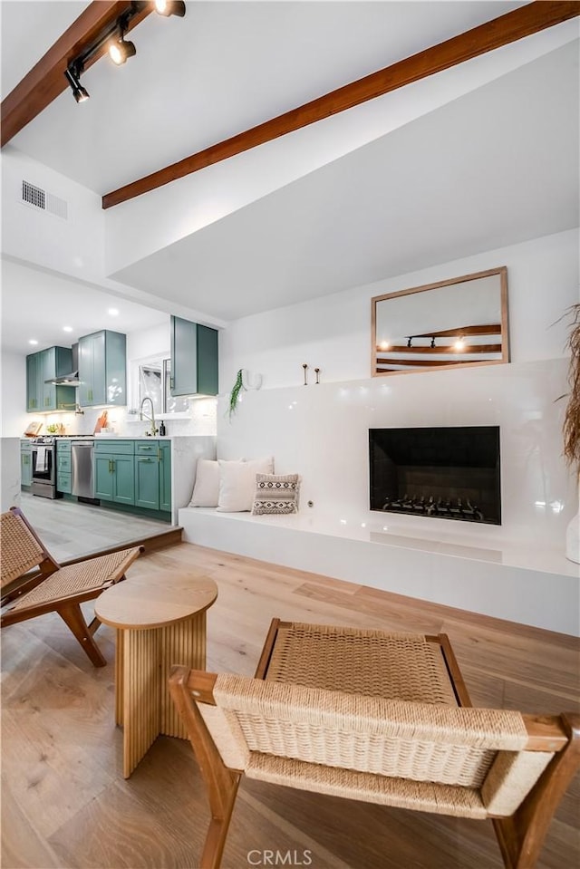 living room featuring beamed ceiling, sink, track lighting, and light hardwood / wood-style floors