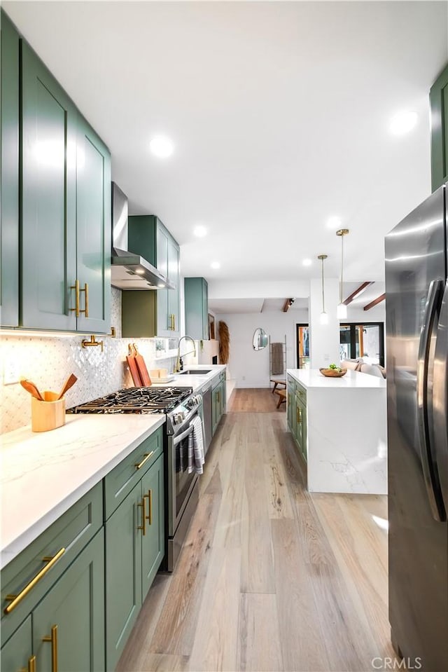 kitchen featuring sink, appliances with stainless steel finishes, green cabinetry, decorative light fixtures, and wall chimney exhaust hood