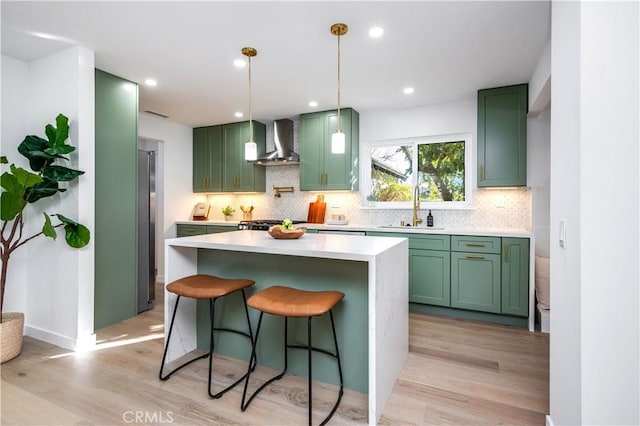 kitchen featuring wall chimney range hood, sink, light hardwood / wood-style flooring, decorative backsplash, and decorative light fixtures