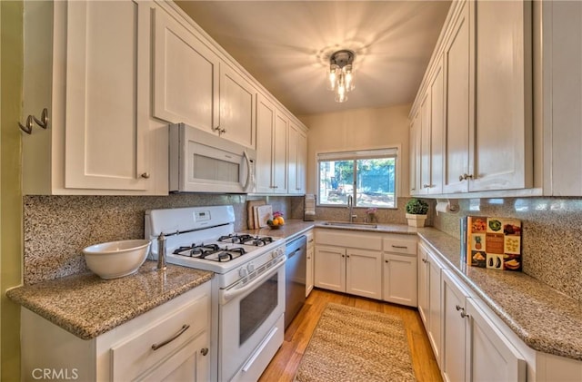 kitchen featuring sink, white cabinetry, tasteful backsplash, white appliances, and light stone countertops