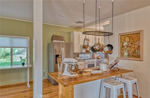 kitchen with stainless steel fridge with ice dispenser, white gas range oven, white cabinets, and a breakfast bar