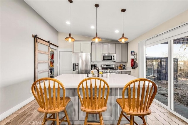 kitchen with gray cabinetry, hanging light fixtures, stainless steel appliances, a barn door, and light wood-type flooring