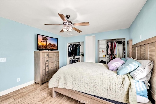 bedroom with two closets, light hardwood / wood-style flooring, and ceiling fan