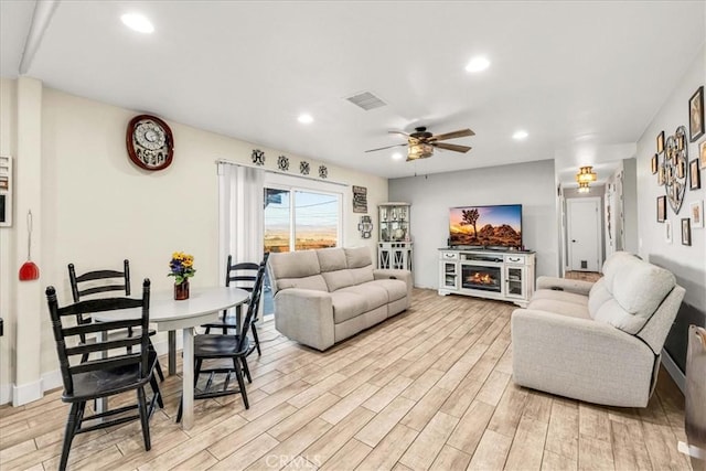 living room with ceiling fan, a fireplace, and light wood-type flooring