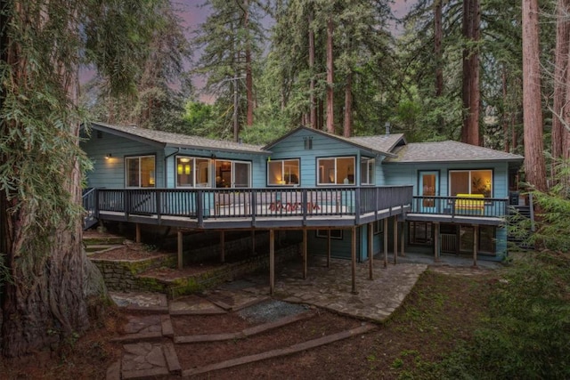 back house at dusk featuring a deck and a patio area