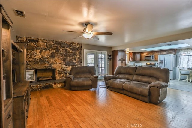 living room featuring french doors, ceiling fan, a stone fireplace, and light wood-type flooring