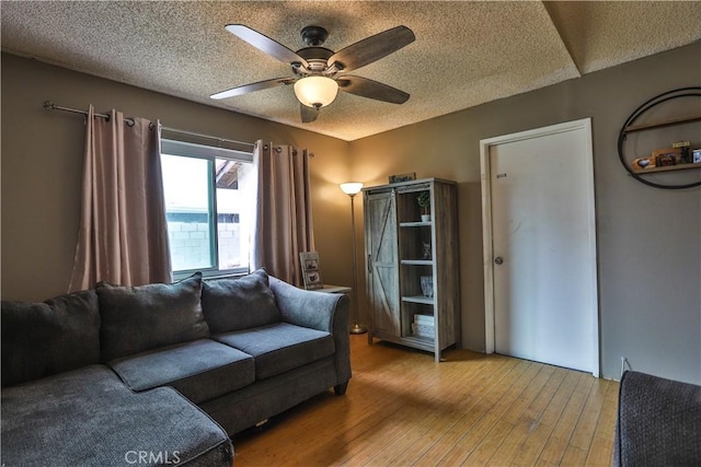 living area with a ceiling fan, a textured ceiling, and wood finished floors