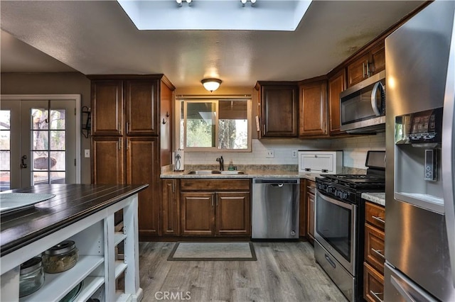 kitchen featuring tasteful backsplash, sink, light stone counters, stainless steel appliances, and light wood-type flooring