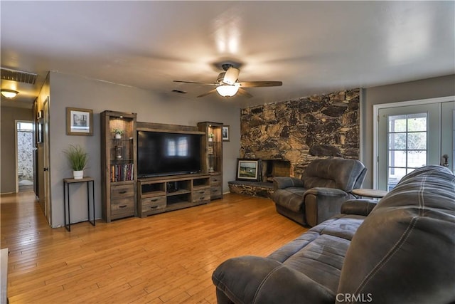 living room featuring light wood-type flooring, visible vents, ceiling fan, and a fireplace