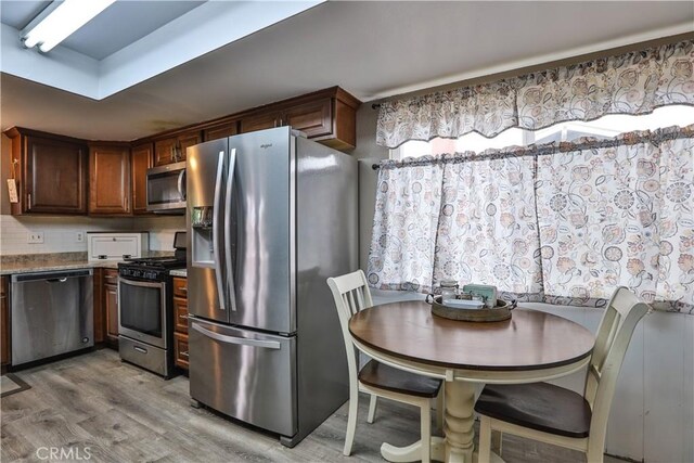 kitchen with light wood-type flooring, light stone countertops, and appliances with stainless steel finishes