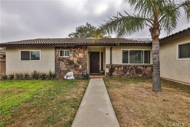 ranch-style house with stone siding, a tiled roof, stucco siding, and a front yard